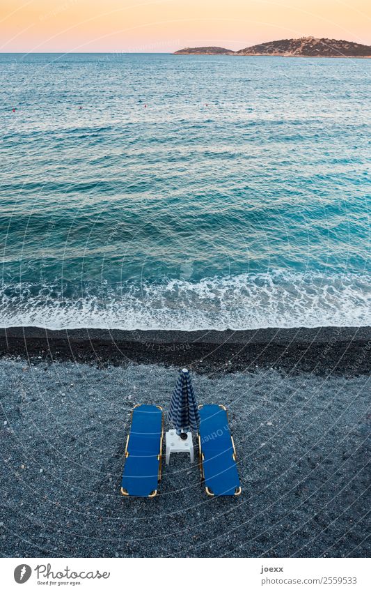 Zwei blaue Strandliegen mit Sonnenschirm und Tischchen am dunklen Strand mit türkisfarbenem Meer vor Sunnenuntergangsstimmung von oben Liegen schwarz Kies
