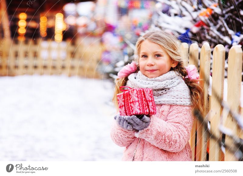 glückliches Kind Mädchen hält Weihnachtsgeschenk im Freien in der Winterstadt kaufen Schnee Dekoration & Verzierung Silvester u. Neujahr Kindheit Pelzmantel