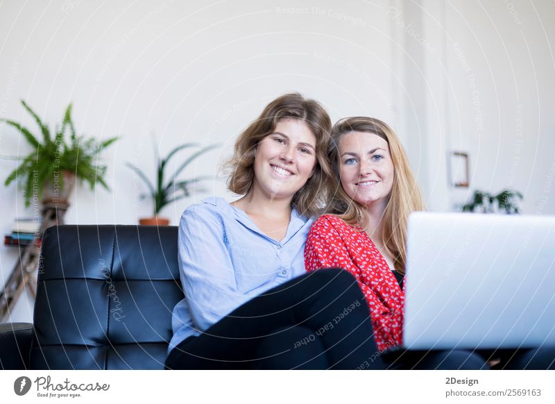 Zwei lächelnde junge Frauen sitzen auf dem Sofa mit Laptop. Lifestyle Glück schön Haus Arbeit & Erwerbstätigkeit Computer Notebook Fotokamera