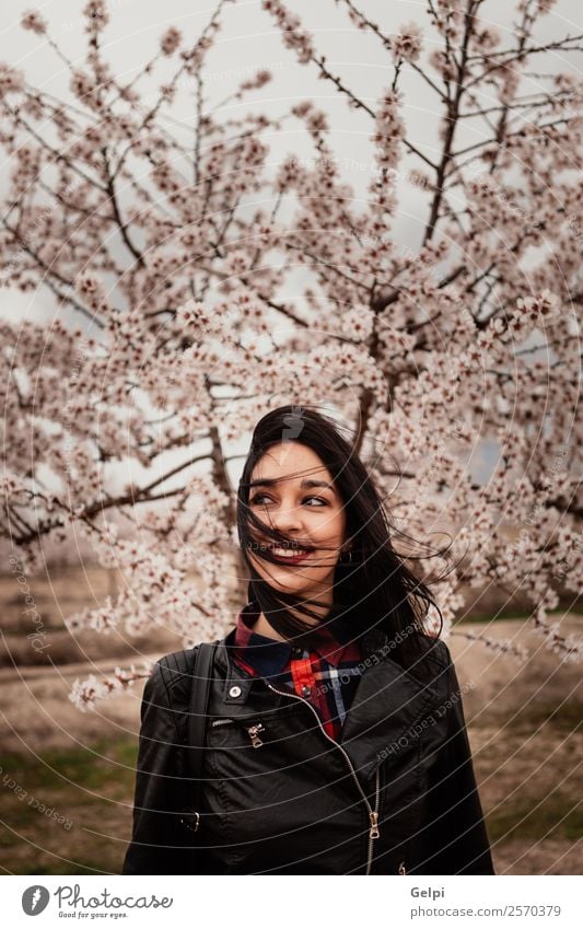Brünettes Mädchen in der Nähe eines Mandelbaums mit vielen Blumen Stil Glück schön Gesicht Garten Mensch Frau Erwachsene Natur Baum Blüte Park Mode Jacke Leder