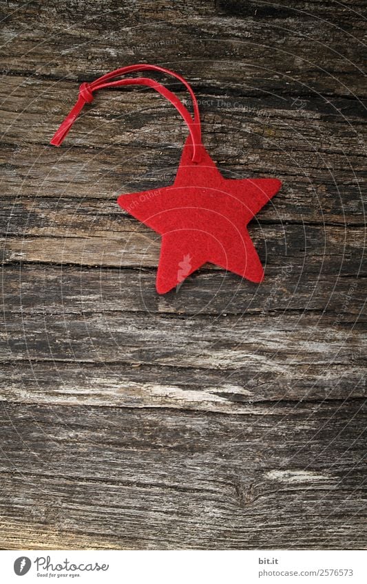 Frohe Weihnachten, ihr Lieben! Roter Stern aus Filz mit kariertem Band, liegt auf altem Holz. Roter Weihnachtsstern, als Dekoration auf rustikalem, braunen Holzbrett. Filz-Stoff-Stern als Schild, Weihnachtsbaum-Anhänger, Geschenkanhänger zur Adventszeit.