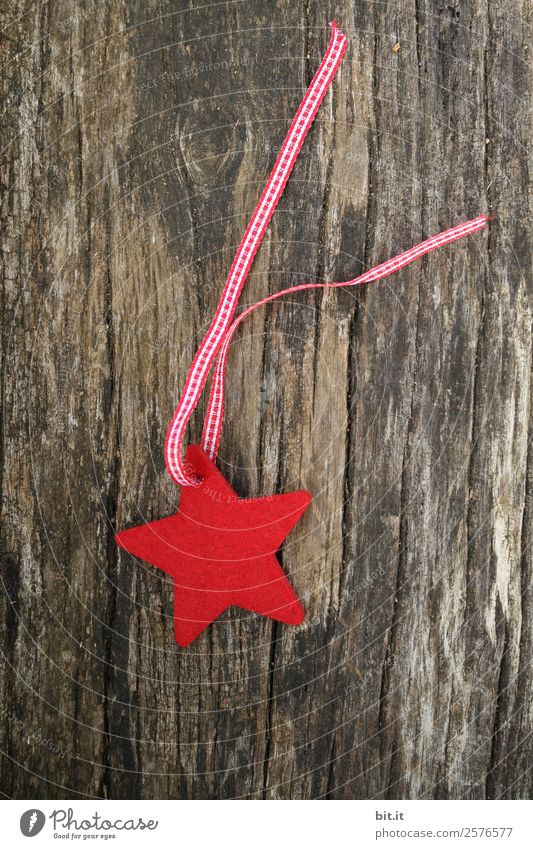 Frohe Weihnachten. Roter Stern aus Filz mit Band, liegt auf altem Holz. Roter Karo-Weihnachtsstern, als Dekoration auf rustikalem, braunen Holzbrett. Filz-Stoff-Stern als Schild, Blanko, Anhänger, Aufhänger auf braunem, rustikalem Holztisch, Textfreiraum.