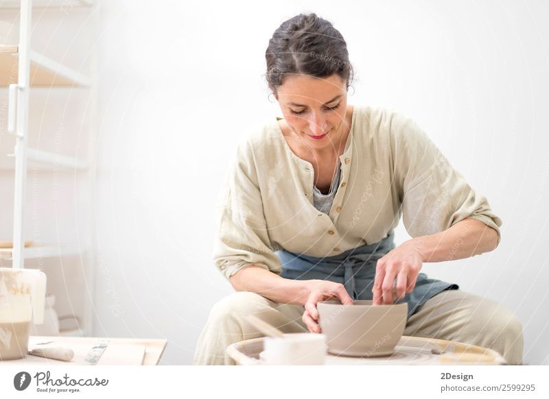 Junge Frau, die an einem Tisch sitzt und Ton oder eine Keramiktasse in ihrem Arbeitsatelier herstellt Geschirr Freizeit & Hobby Handarbeit