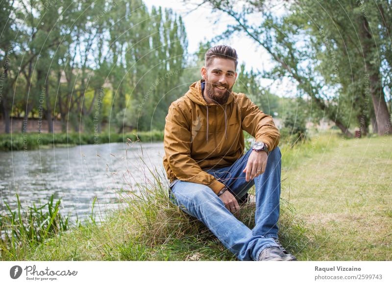 Lächelnder junger Mann, der am Flussufer sitzt. Lifestyle Leben Junger Mann Jugendliche 1 Mensch 18-30 Jahre Erwachsene Natur Herbst Schönes Wetter Gras