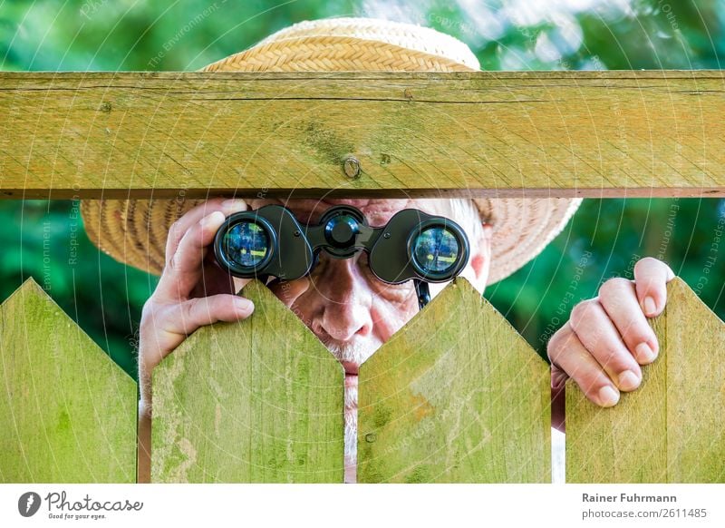 ein Mann blickt mit einem Fernglas durch einen Zaun Mensch maskulin Erwachsene Männlicher Senior 1 "Zaun Lattenzaun" Hut beobachten Neugier gereizt