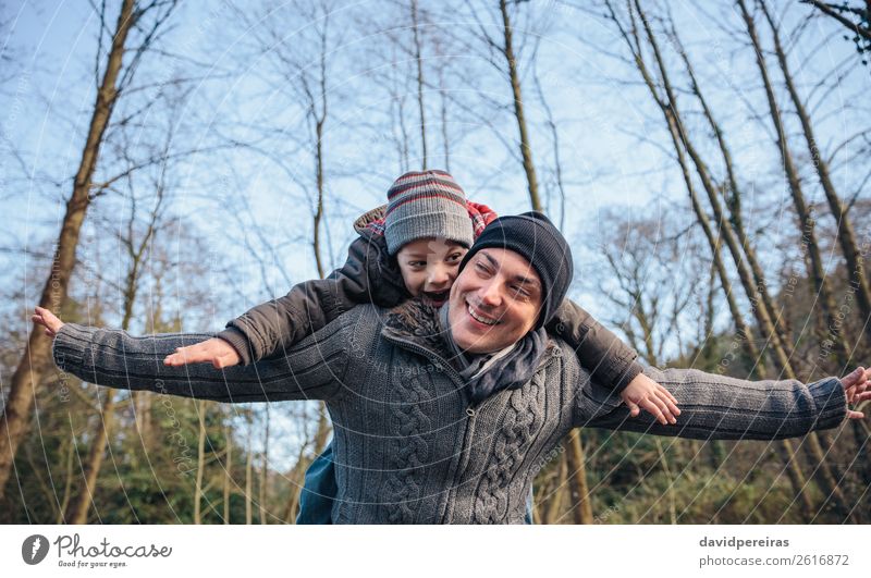 Mann, der dem glücklichen Kind im Wald eine Huckepackfahrt anbietet. Lifestyle Freude Glück Freizeit & Hobby Spielen Winter Junge Erwachsene Eltern Vater