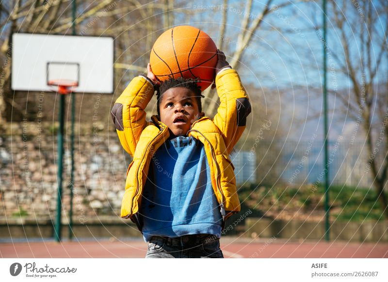 Niedlicher kleiner Junge, der einen Basketball hält und versucht, ein Tor zu erzielen Freude Glück Erholung Freizeit & Hobby Spielen Winter Sport Kind Schule