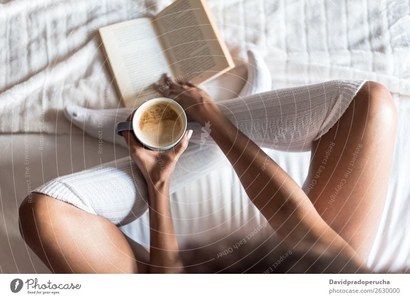 Frau liest ein Buch und trinkt Kaffee auf dem Bett mit Socken. 