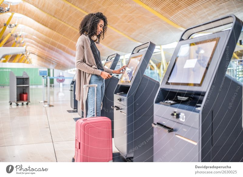 glückliche schwarze Frau, die den Check-in-Automaten am Flughafen benutzt, um die Bordkarte zu bekommen. Selbst Aufschlag kariert Selbstbedienung Eintrittskarte