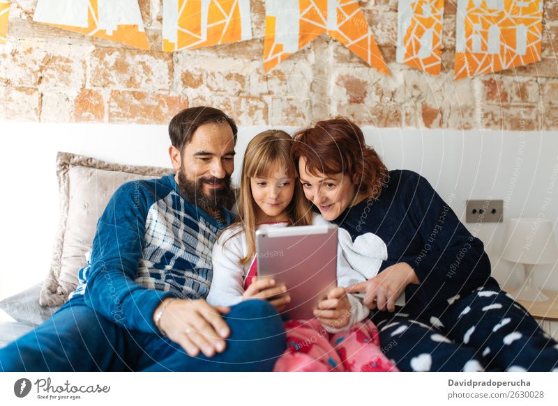 Ein Paar entspannt zu Hause im Bett mit seiner kleinen Tochter auf dem Handy und Tablett. Zuneigung Schlafzimmer Ehefrau Ehemann Kind Mobile Telefon