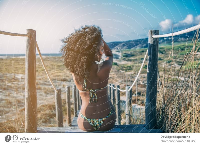 Schöne junge schwarze Frau, die in einer hölzernen Fußgängerbrücke am Strand sitzt. Hintergrundbild Bikini Brücke Küste krause Haare Ausflugsziel Behaarung