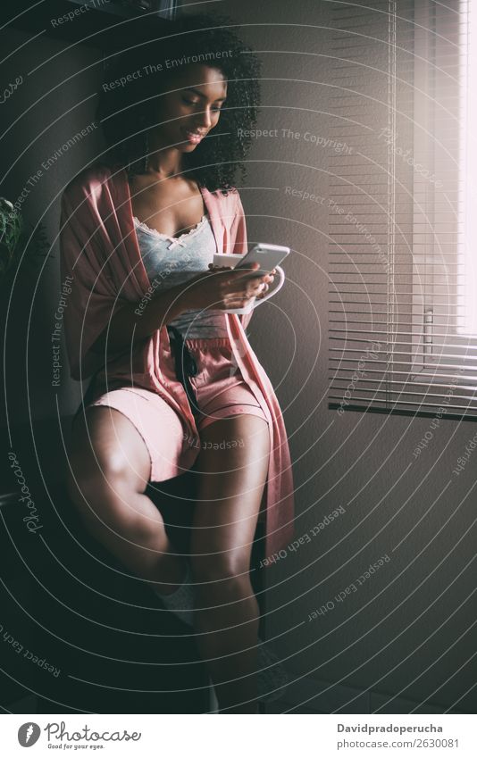 hübsche schwarze Frau am Fenster sitzend mit Tasse Kaffee und Smartphone Tee hintergrundbeleuchtet PDA Technik & Technologie Telefon Mobile Mitteilung Drahtlos
