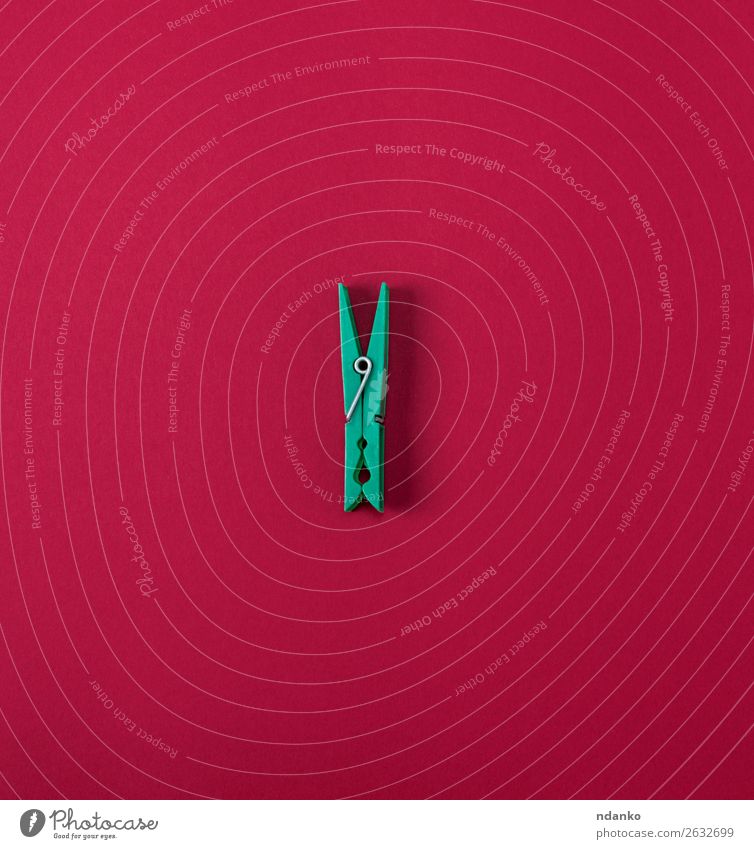 Grüne Plastikklemme auf rotem Hintergrund Werkzeug Bekleidung Stoff Kunststoff hell grün Farbe Stecknadel Objektfotografie Wäscheklammern Magazin Haushalt