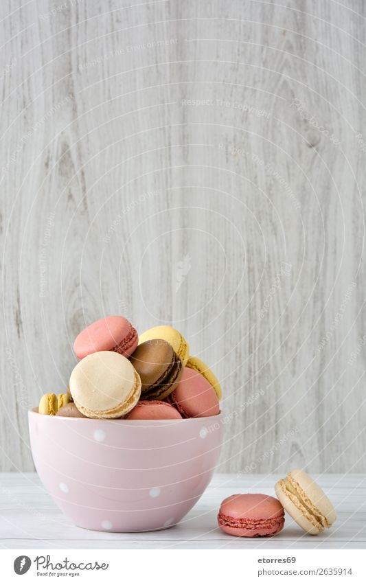 Bunte Makronen in einer Schleife auf weißem Holztisch Macaron Erdbeeren Zitrone Dessert Kaffee gelb Schokolade Konfekt Himbeeren Tradition Süßwaren
