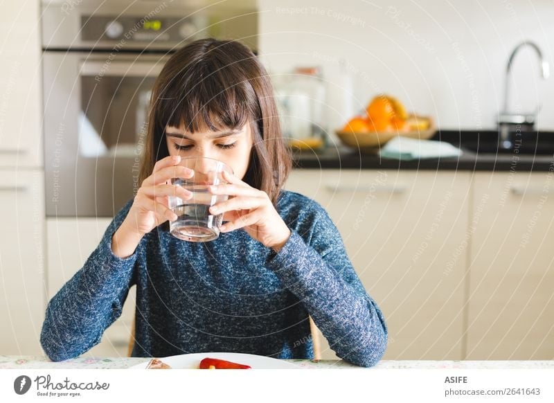 Süßes durstiges Mädchen trinkt Wasser im Glas zu Hause. Ernährung Essen Mittagessen Abendessen trinken Freude Glück schön Tisch Küche Kind sitzen niedlich