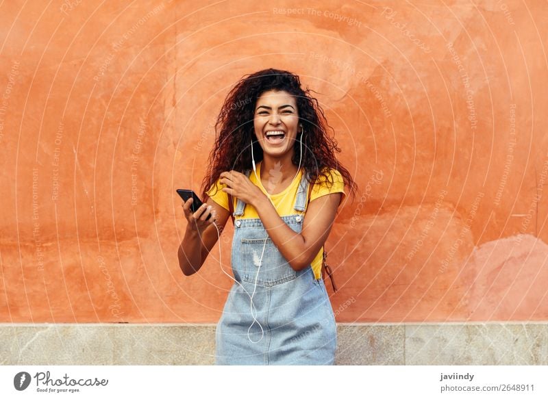 Junge arabische Frau lacht und hört Musik mit Kopfhörern im Freien Lifestyle Haare & Frisuren Telefon Technik & Technologie Mensch feminin Junge Frau