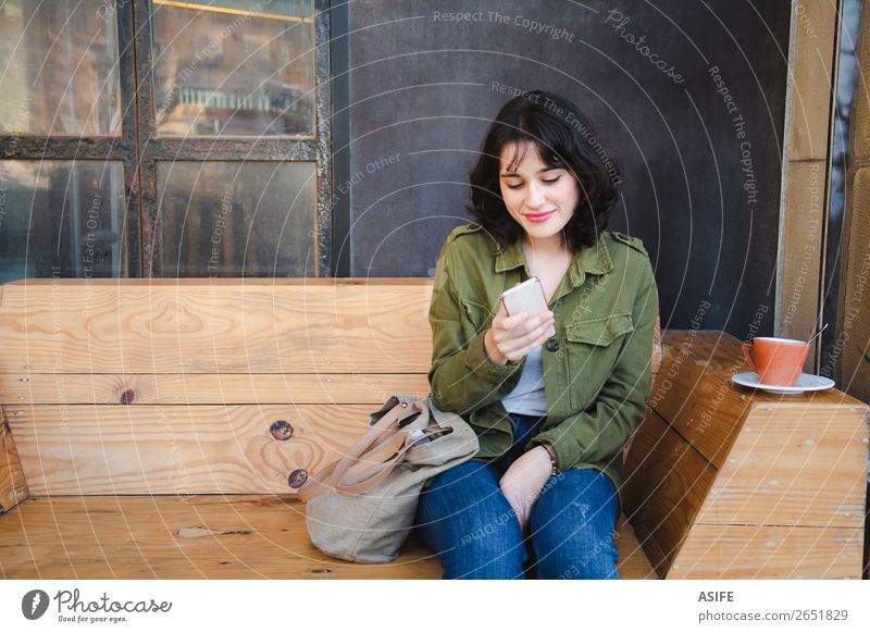 Junge Frau benutzt ihr Handy im Café. Kaffee Glück schön Freizeit & Hobby Tafel Telefon PDA Technik & Technologie Erwachsene Terrasse Jeanshose Jacke brünett