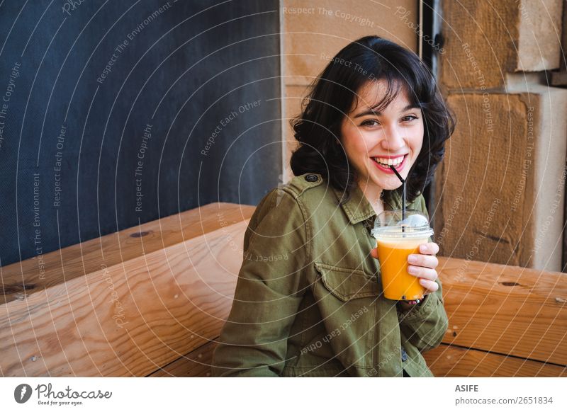 Fröhliche junge Frau trinkt einen Frucht-Smoothie in einer Bar-Terrasse. Gemüse trinken Saft Lifestyle Freude Glück schön Erwachsene Container Jacke brünett