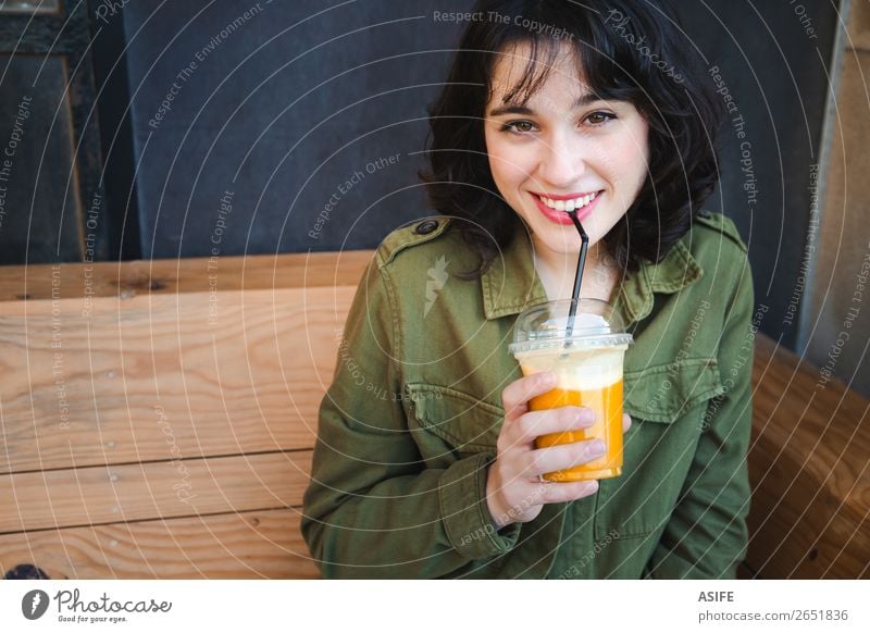 Schöne Frau trinkt einen Frucht-Smoothie im Freien. Gemüse trinken Saft Lifestyle Freude Glück schön Erwachsene Terrasse Container Jacke brünett Holz Kunststoff