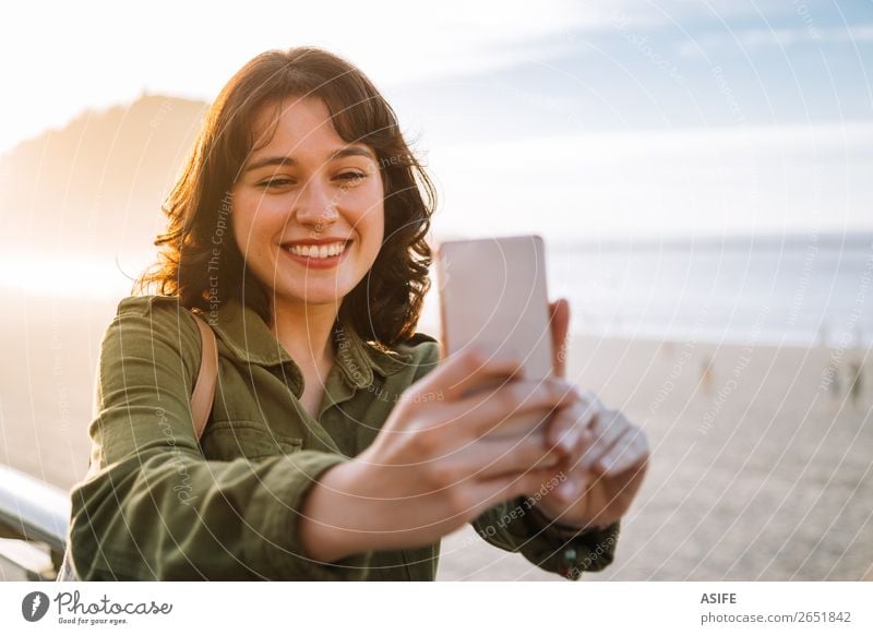 Junge glückliche Frau mit grüner Jacke macht ein Selfie mit ihrem Smartphone am Strand bei Sonnenuntergang Glück schön Freizeit & Hobby Ferien & Urlaub & Reisen