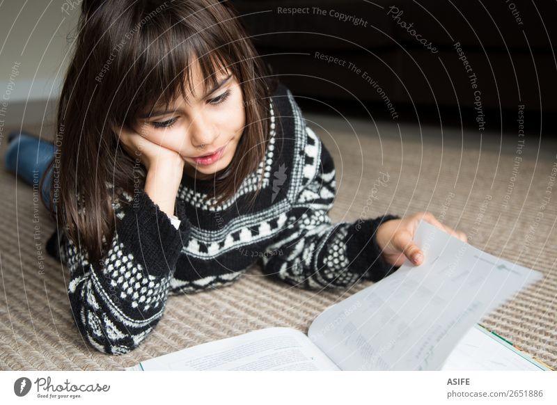 Niedliches kleines Mädchen liegt auf dem Teppich und liest ein Buch Lifestyle Freude Glück schön Erholung Freizeit & Hobby lesen Kind Schule Mensch Frau