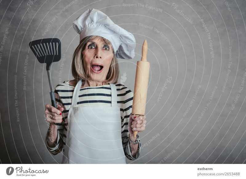ältere Frau mit Kochmütze und Nudelholz und Spachtel auf grauem Hintergrund Ernährung Diät Lifestyle Freizeit & Hobby Küche Restaurant Ruhestand feminin