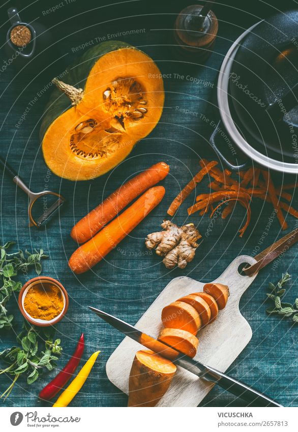 Zutaten für eine gesunde Suppe oder einen Gemüseeintopf mit orangefarbenen vegetarischen Zutaten: Kürbis, Karotten, Süßkartoffeln, Kurkuma, Ingwer und Chili auf dem Küchentisch im Hintergrund, Ansicht von oben.