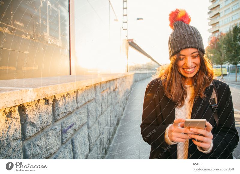 Glückliche junge Frau mit ihrem Handy auf der Straße Lifestyle Freude schön lesen Sonne Winter Telefon PDA Technik & Technologie Internet Erwachsene Jugendliche