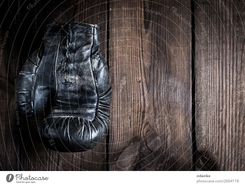 sehr alter schwarzer Boxhandschuh aus Leder mit Schnürung Lifestyle Fitness Sport Handschuhe Holz dunkel retro braun Schutz Aggression Konkurrenz eine Boxsport