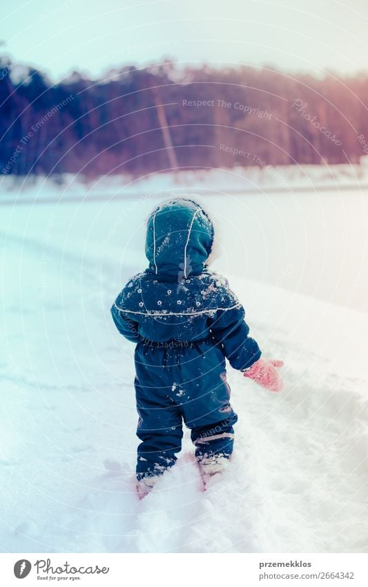 Kleines Mädchen genießt den Winter bei einem Spaziergang durch tiefen Schnee. Kleinkind spielt im Freien, während Schnee fällt. Das Kind trägt einen dunkelblauen Schneeanzug und eine Wollmütze