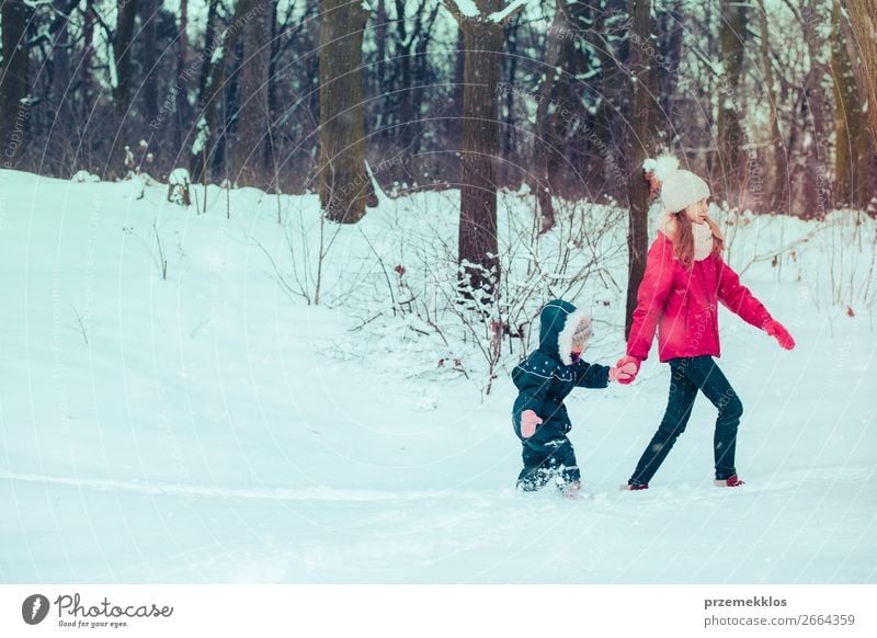 Teenager-Mädchen genießt den Schnee mit ihrer kleinen Schwester. Kinder gehen durch tiefen Schnee, während Schnee fällt, genießen Winterzeit. Sisters verbringen Zeit miteinander. Mädchen tragen Winterkleidung, junges Mädchen trägt rosa Mantel und Wollmütze