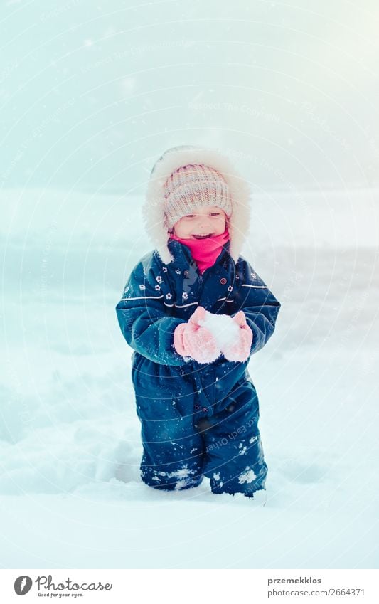 Fröhliches kleines Mädchen genießt den Schnee. Kind, das draußen spielt und im Winter bei Schneefall durch tiefen Schnee läuft. Kleinkind trägt dunkelblauen Schneeanzug