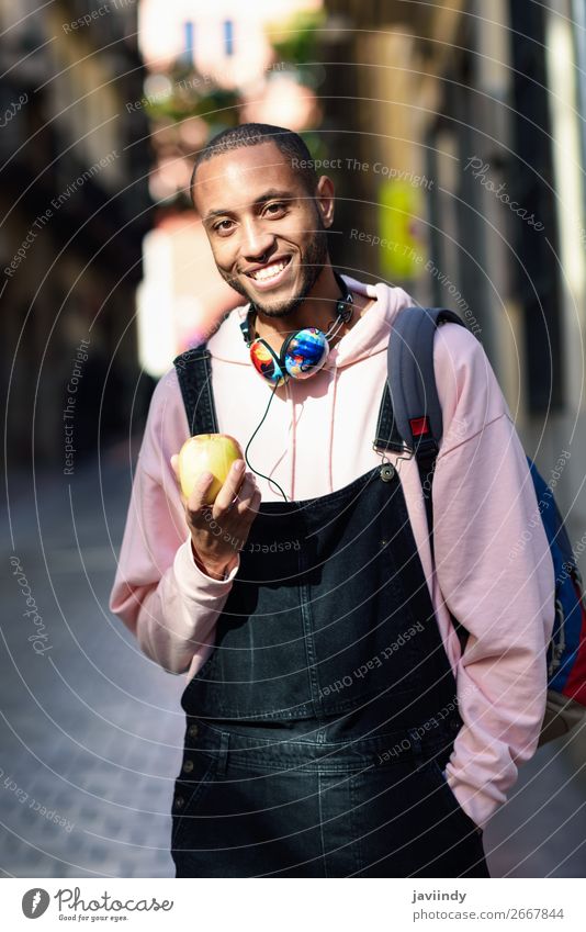 Junger schwarzer Mann, der einen Apfel isst, der die Straße entlang läuft. Frucht Essen Lifestyle Glück schön Mensch maskulin Junger Mann Jugendliche Erwachsene