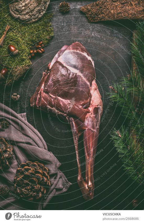 Rohe gealterte Rehkeule mit Knochen auf dunklem Küchentisch-Hintergrund, Ansicht von oben. Rohes Fleisch der Rehkeule. Kochen Vorbereitung der Hirschbraten roh