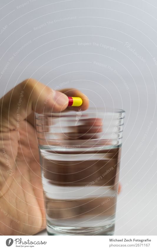 Männer geben eine rot-gelbe Pille in einem Glas Wasser. Schalen & Schüsseln Behandlung Krankheit Medikament Wissenschaften Hand Holz blau rosa weiß Farbe zeigen