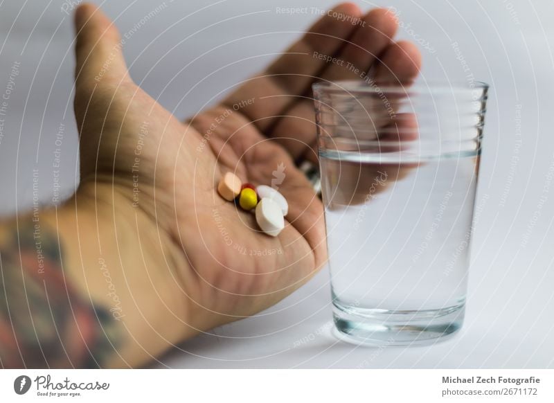 Männer, die Pillen in verschiedenen Farben neben einem Glas Wasser zeigen. Schalen & Schüsseln Behandlung Krankheit Medikament Wissenschaften Hand Holz blau