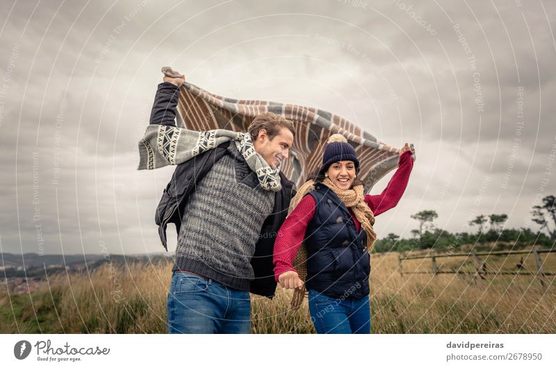 Junges Paar, das an einem windigen Tag im Freien mit Decke spielt. Lifestyle Glück schön Spielen Meer Winter Berge u. Gebirge Frau Erwachsene Mann Natur Himmel