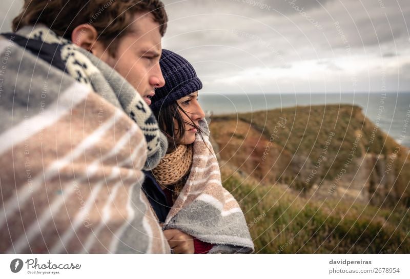 Junges Paar unter der Decke, das an einem kalten Tag auf das Meer schaut. Lifestyle schön Winter Frau Erwachsene Mann Natur Himmel Wolken Herbst Wind Wiese