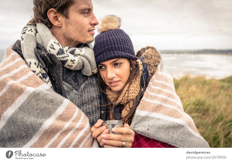 Junges Paar, das sich an einem kalten Tag unter der Decke im Freien umarmt. Getränk Kaffee Tee Lifestyle Glück Meer Winter Berge u. Gebirge Frau Erwachsene Mann