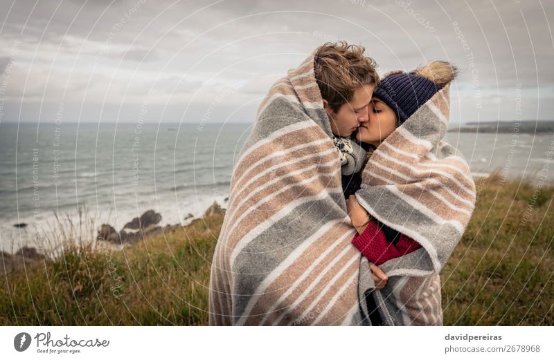 Junges Paar, das sich an einem kalten Tag unter der Decke im Freien küsst. Lifestyle Glück schön Meer Winter Berge u. Gebirge Frau Erwachsene Mann Natur Himmel
