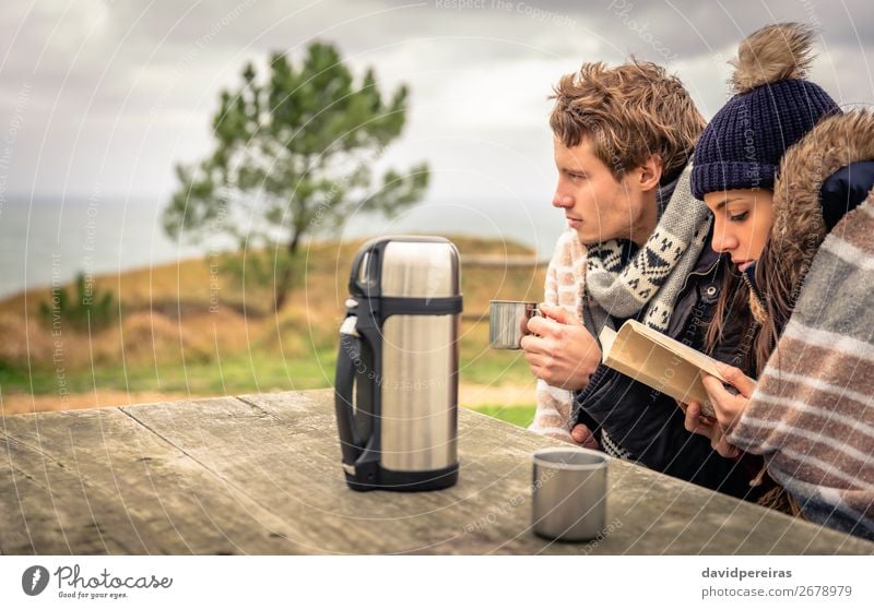 Junges Paar in einem kalten Tag mit bewölktem Himmel auf dem Hintergrund Getränk Kaffee Tee Lifestyle Glück lesen Meer Winter Tisch Frau Erwachsene Mann Hand