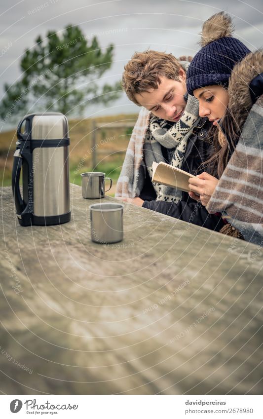 Junges Paar unter der Decke liest Buch im Freien an einem kalten Tag. Getränk Kaffee Tee Lifestyle lesen Abenteuer Winter Berge u. Gebirge Tisch Frau Erwachsene