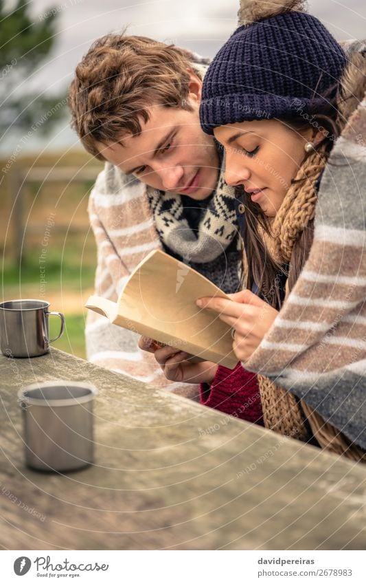 Junges Paar unter der Decke liest Buch im Freien an einem kalten Tag. Getränk Kaffee Tee Lifestyle Glück lesen Meer Winter Berge u. Gebirge Tisch Frau