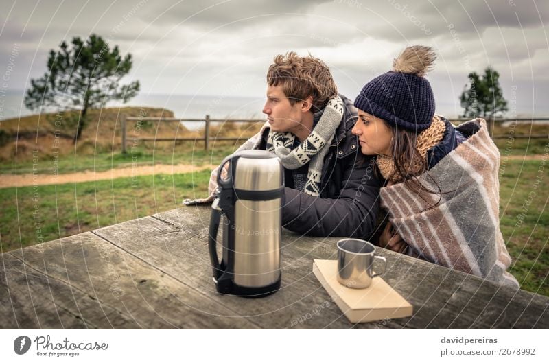 Junges Paar unter der Decke, das an einem kalten Tag auf das Meer schaut. Getränk Kaffee Tee Lifestyle Glück Winter Berge u. Gebirge Tisch Frau Erwachsene Mann