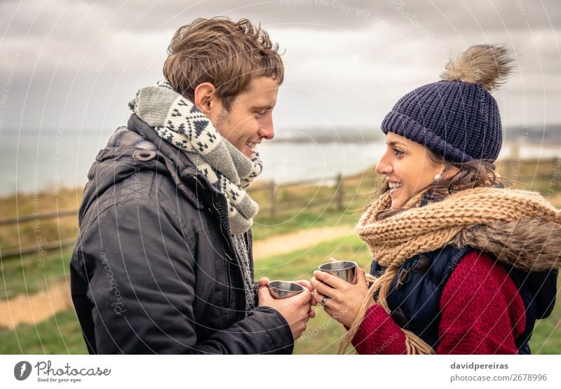 Junges Paar, das an einem kalten Tag im Freien Tassen mit heißen Getränken hält. Kaffee Tee Lifestyle Glück Meer Winter Berge u. Gebirge Frau Erwachsene Mann