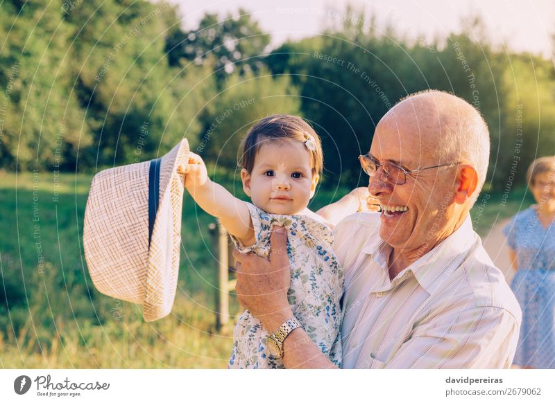 Kleines Mädchen spielt mit dem Hut eines älteren Mannes im Freien. Lifestyle Glück Erholung Spielen Sommer Mensch Baby Kleinkind Frau Erwachsene Eltern