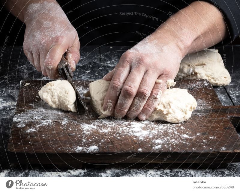Chefkoch schneidet Weizenmehlteig in Stücke. Teigwaren Backwaren Brot Ernährung Tisch Küche Koch Mensch Mann Erwachsene Hand Holz machen schwarz weiß Tradition