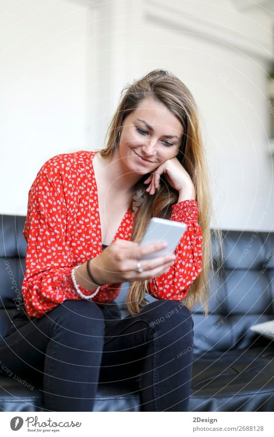 Blondes Mädchen, das ein Smartphone benutzt, während es auf einem Ledersofa sitzt. schön Haare & Frisuren Sofa Wohnzimmer Telefon Handy PDA