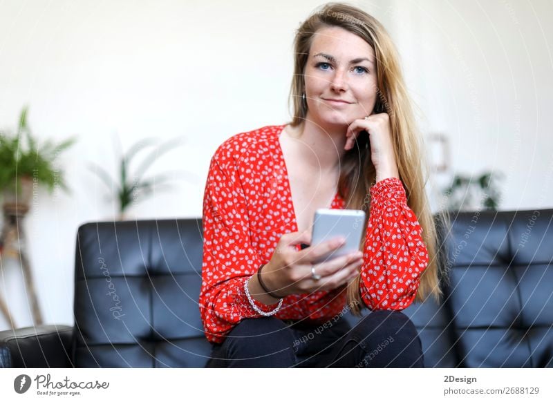 Blondes Mädchen, das ein Smartphone benutzt, während es auf dem Sofa sitzt. schön Haare & Frisuren Wohnzimmer Telefon Handy PDA Technik & Technologie feminin