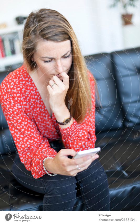 Junge Frau, die Nägel kaut, während sie auf einer Ledercouch sitzt. Lifestyle schön Haare & Frisuren Sofa Telefon PDA Technik & Technologie Mensch Erwachsene